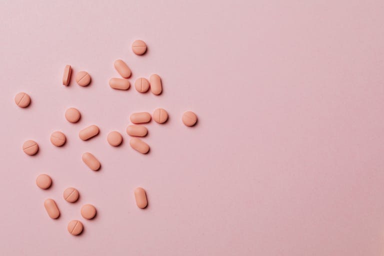 Flat lay of pink pills scattered on a pink background, conveying healthcare themes.